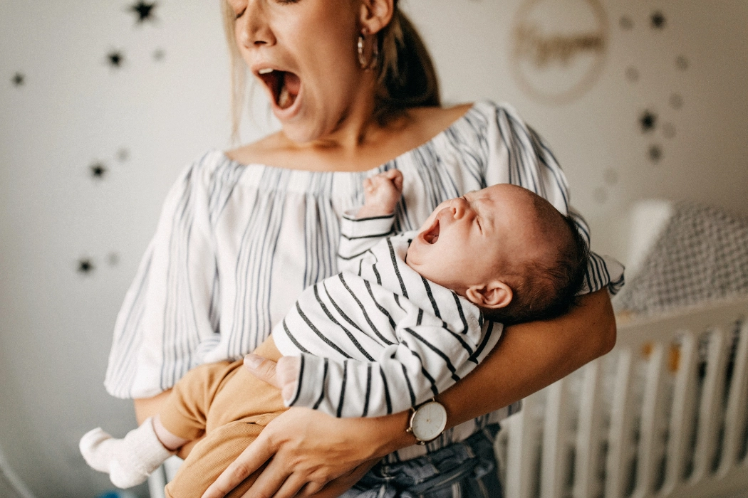 Worn out mother, yawning while holding her baby.